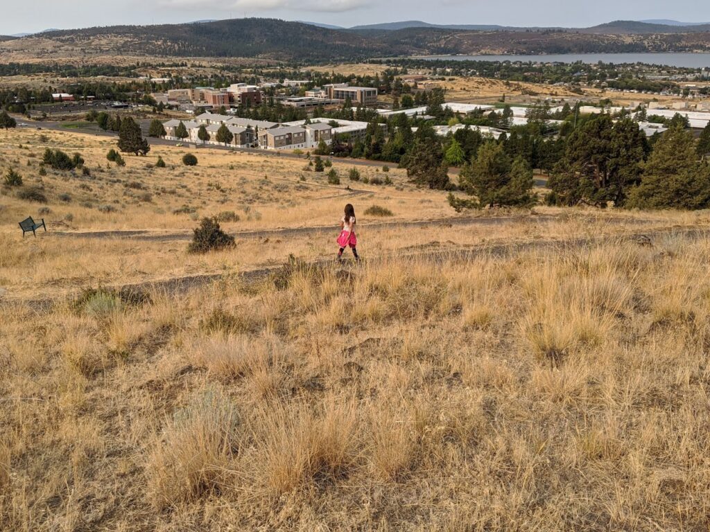 Girl walking on trail with a city and lake view.